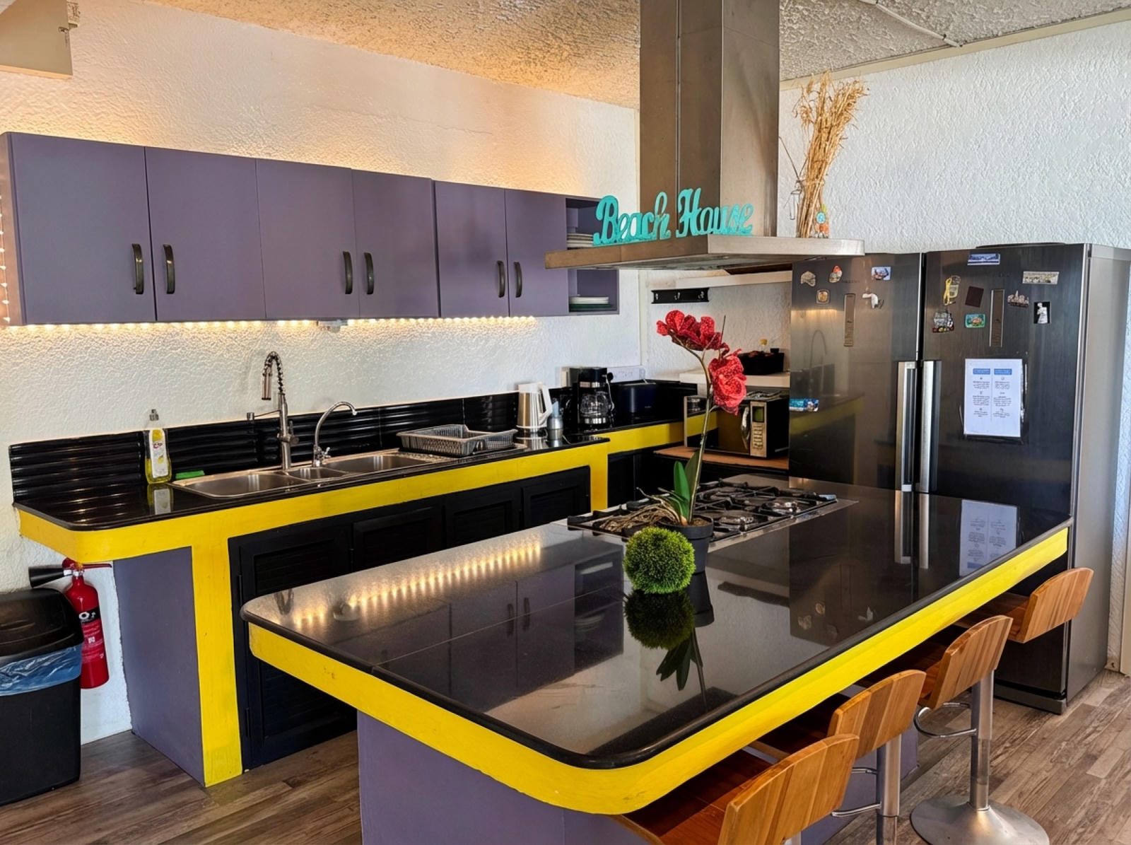 Yellow and purple kitchen with Beach House neon sign and bar stools